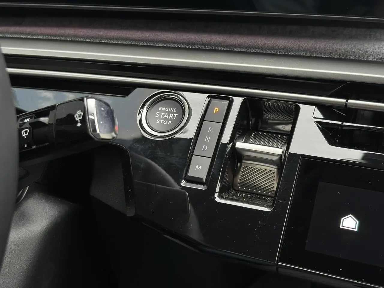 Gros plan sur la console centrale noire brillante du Peugeot 3008 Hybrid 145 avec bouton start/stop et commande de boîte automatique.