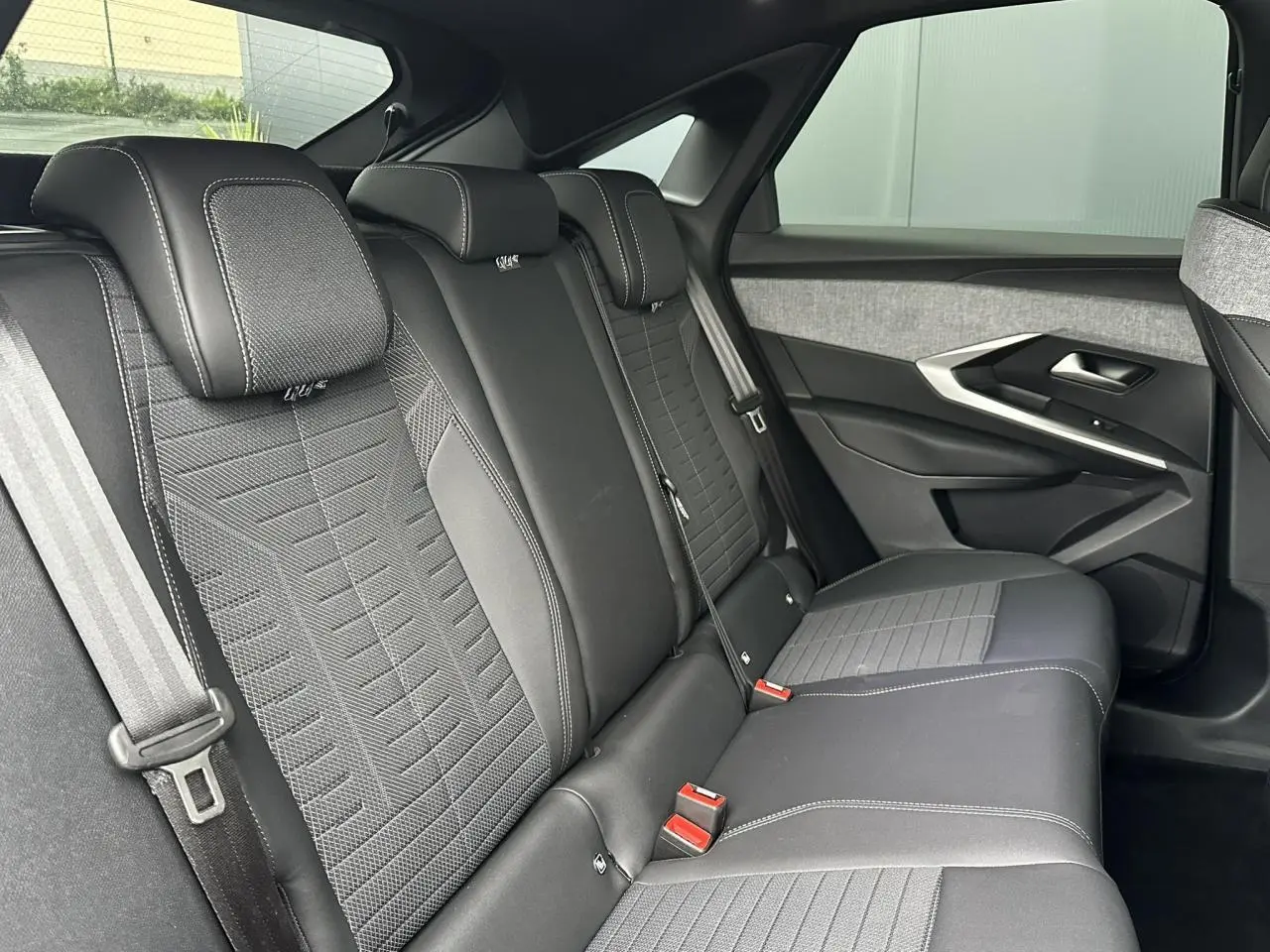 Vue latérale droite des sièges arrière noirs et gris du Peugeot 3008 Hybrid 2024 avec surpiqûres blanches et ceintures visibles.