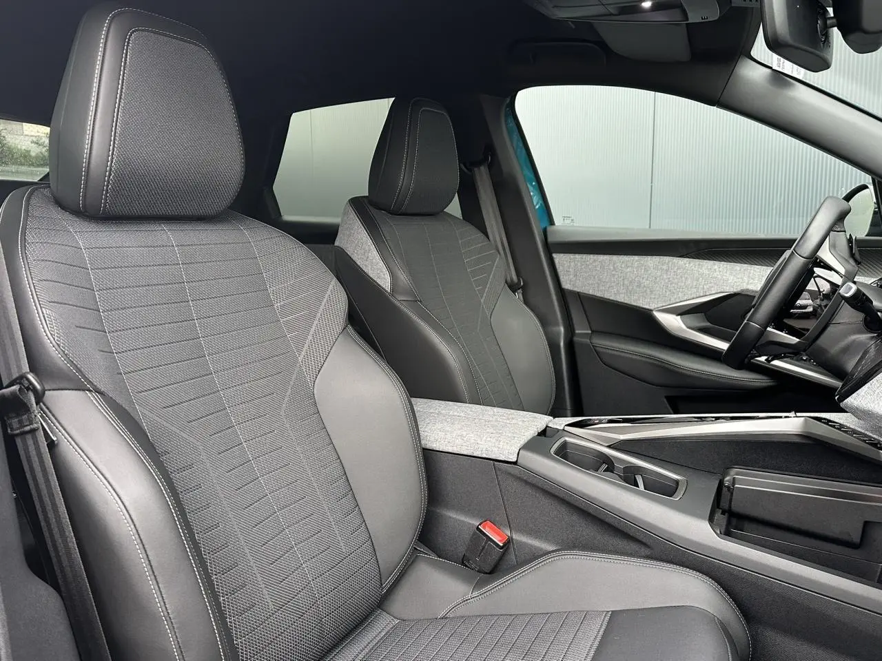 Intérieur du Peugeot 3008 Hybrid 2024, vue côté conducteur, sièges tissu gris avec surpiqûres claires et console centrale.