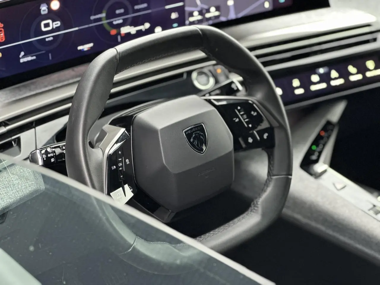 Volant compact cuir noir avec commandes intégrées et logo Peugeot, tableau de bord numérique panoramique en arrière-plan