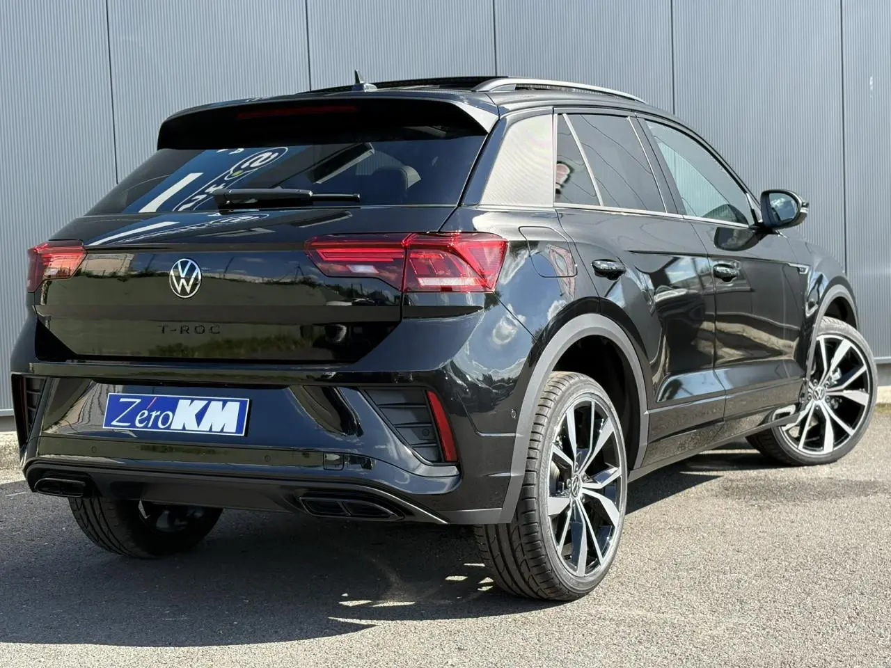 Volkswagen T-Roc noir Grenadilla en 3/4 arrière droit, jantes alliage 19 pouces et toit ouvrant visible.