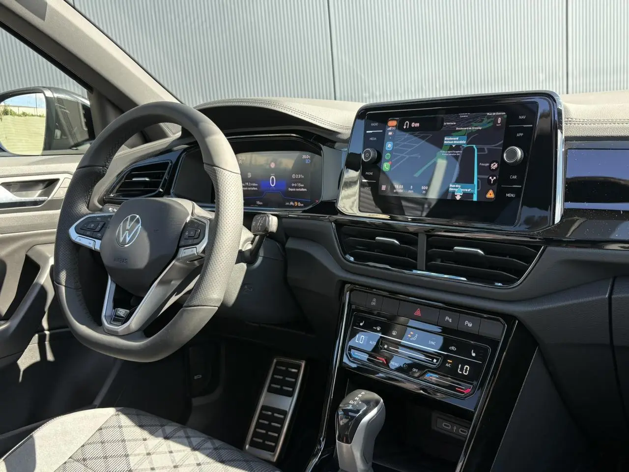 Intérieur du Volkswagen T-Roc 2025 vu côté conducteur, volant cuir avec logo VW et écran tactile de navigation allumé.