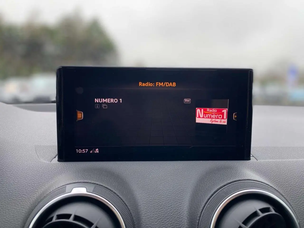 Écran central de l'Audi Q2 2023 affichant la radio FM/DAB, avec deux aérateurs ronds en aluminium visibles en dessous.