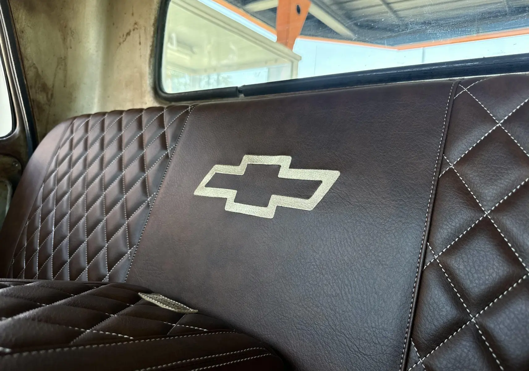 Gros plan sur la banquette arrière en cuir marron matelassé avec logo Chevrolet brodé, intérieur d’un C10 1963.