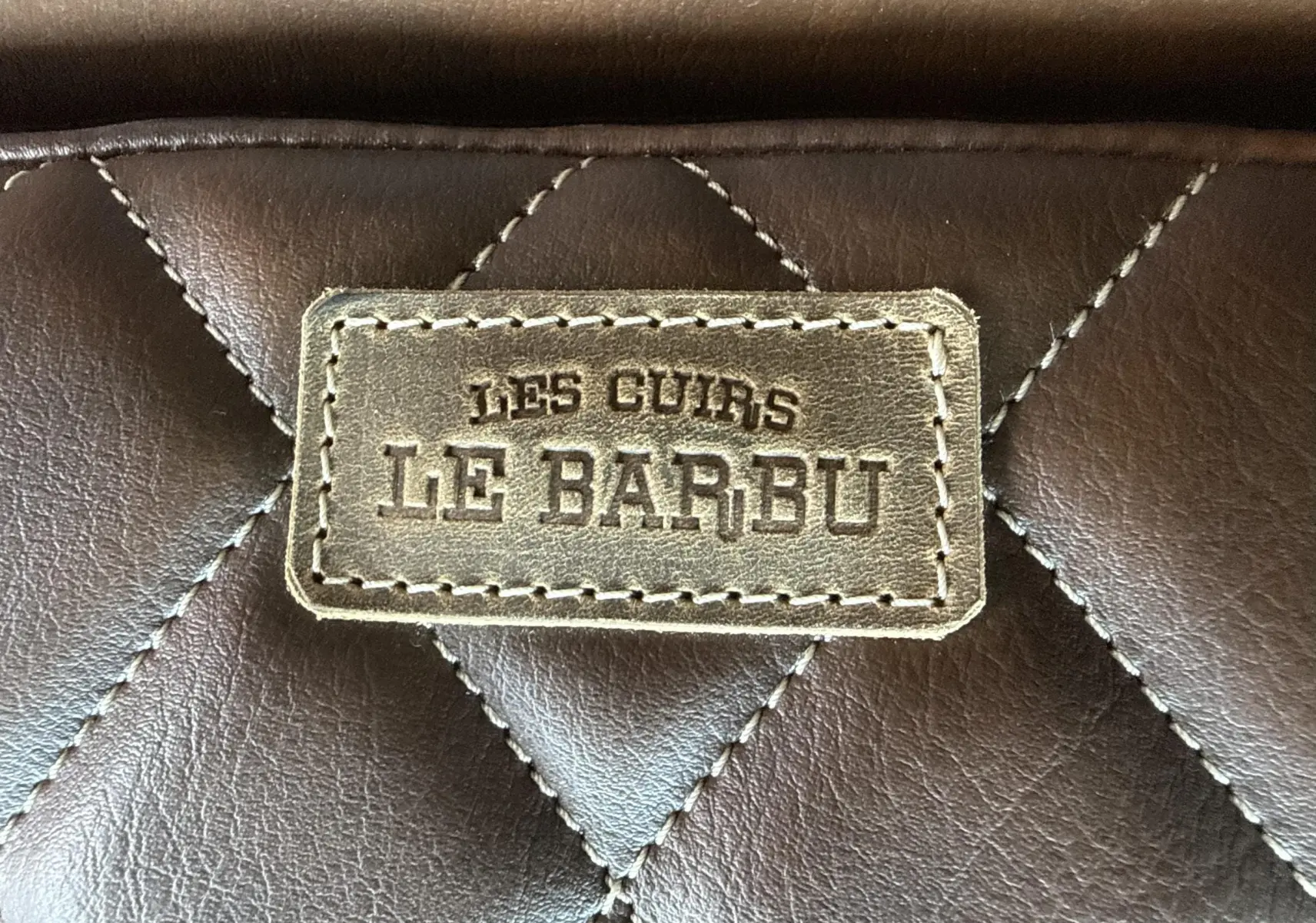 Gros plan sur une étiquette en cuir marron matelassé avec l'inscription "LES CUIRS LE BARBU".