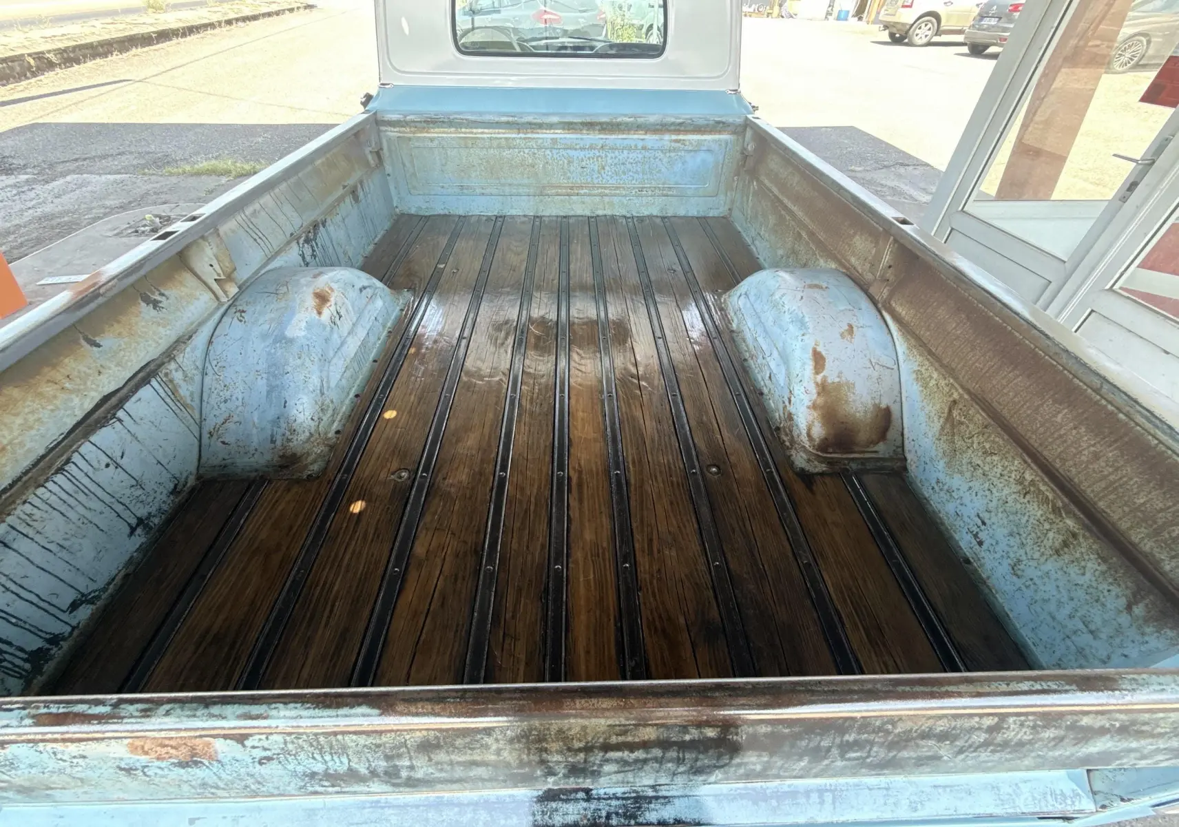 Vue plongeante sur la benne en bois patiné du pick-up Chevrolet C10 Apache 1963 bleu, montrant l'usure et la rouille.