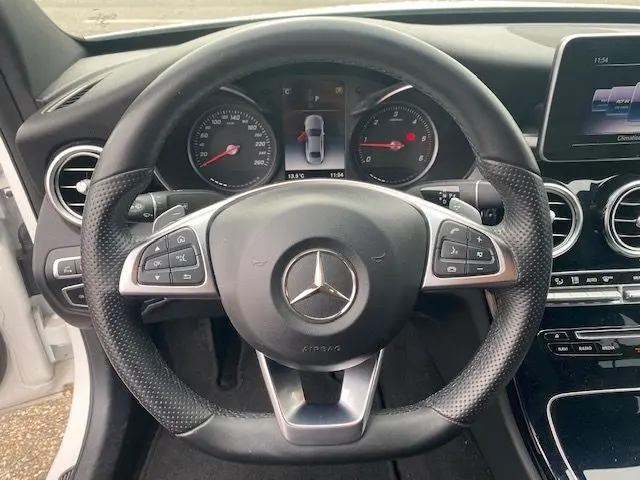 Vue rapprochée du volant en cuir perforé d'une Mercedes Classe C 250D 2018 avec tableau de bord numérique et commandes intégrées.