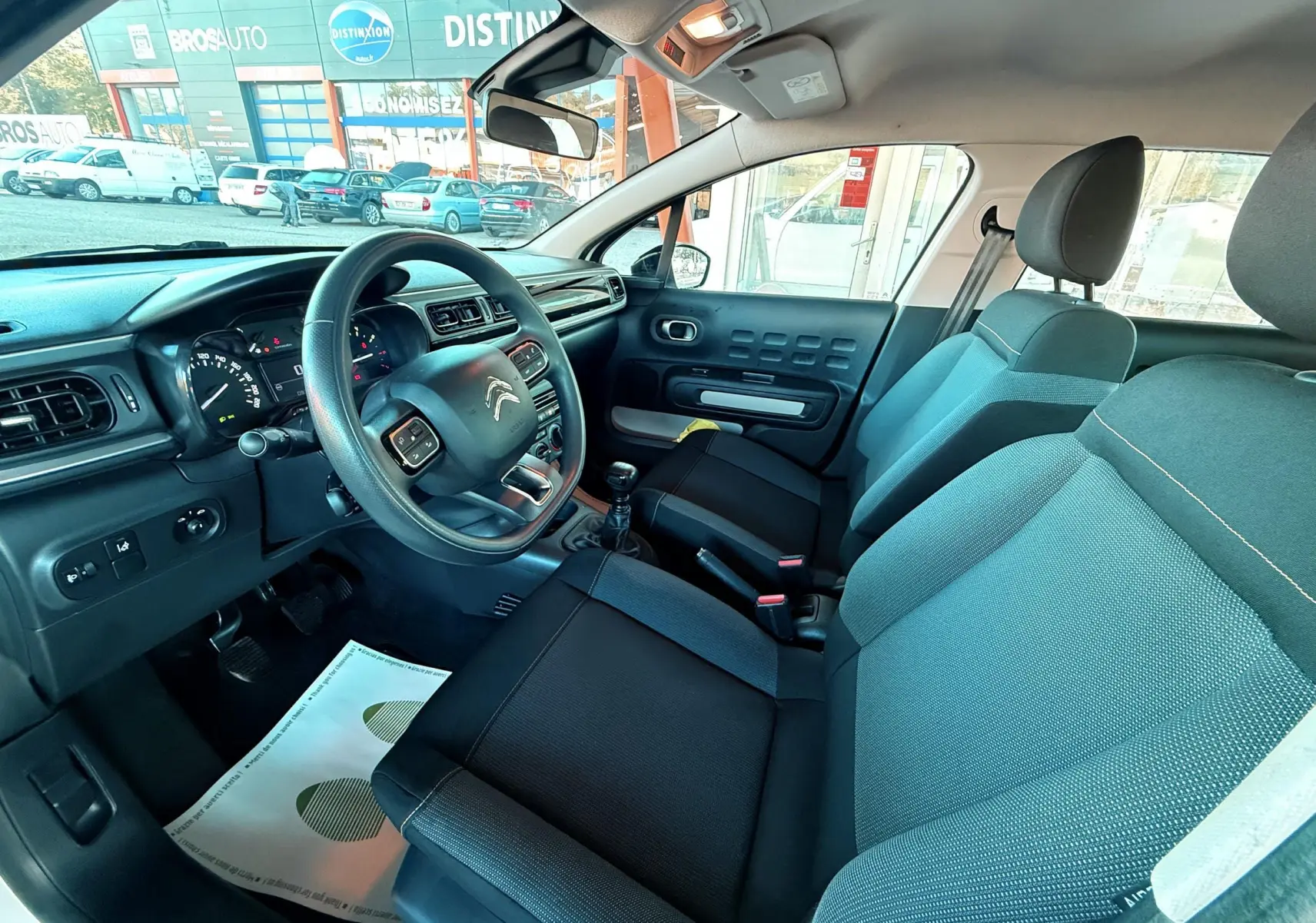 Intérieur de la Citroën C3 blanc, vue côté conducteur, montrant le volant, tableau de bord et sièges noirs et gris.