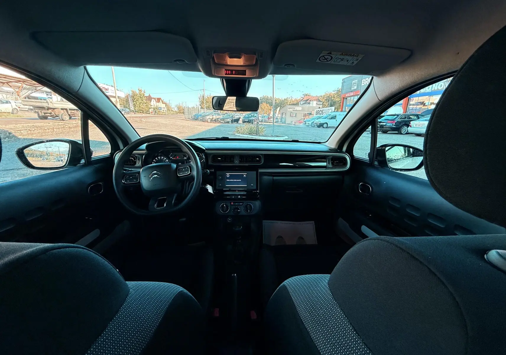 Vue intérieure avant du poste de conduite d'une Citroën C3 blanche, avec tableau de bord et volant visibles.