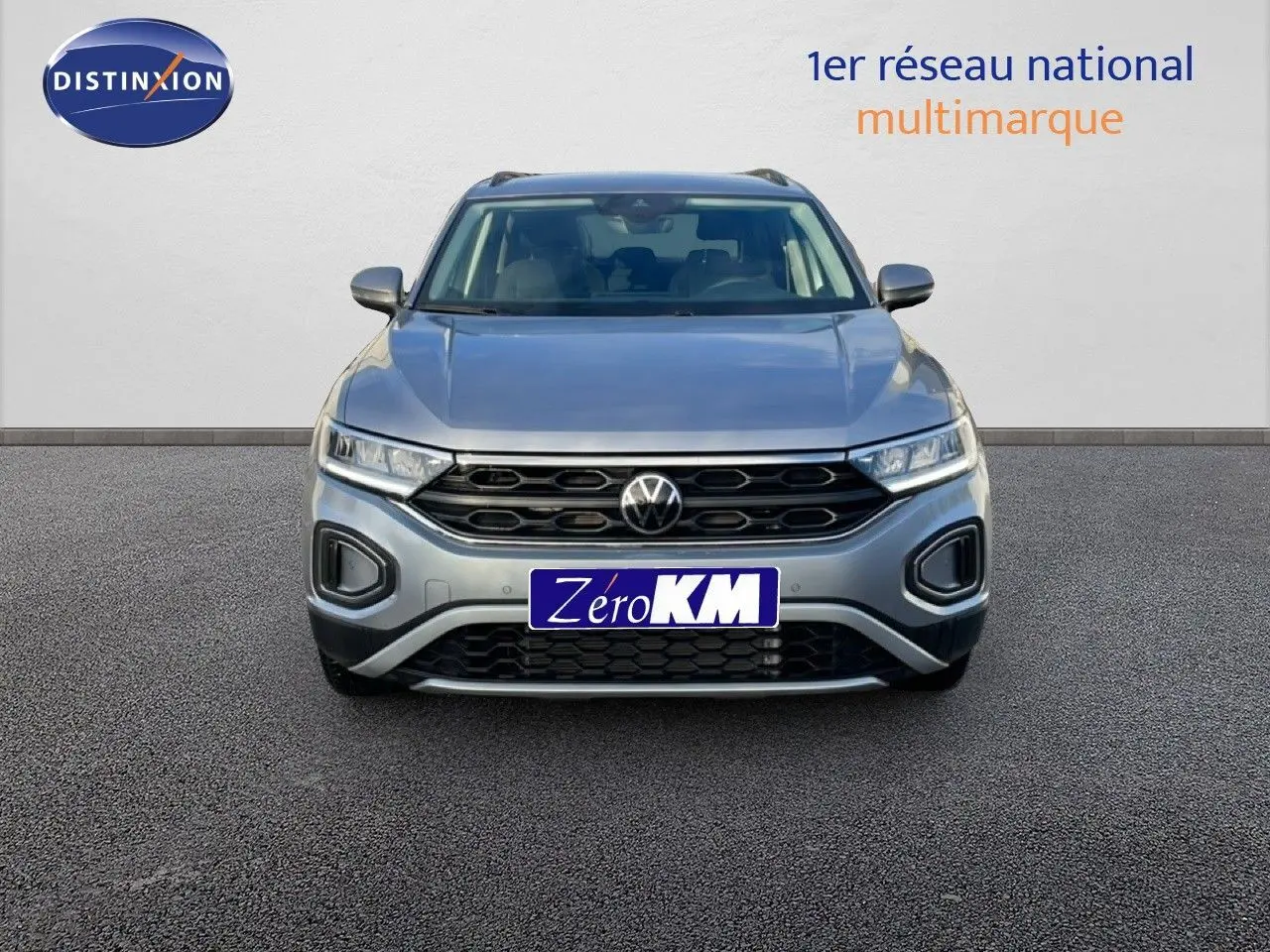 Vue frontale d'un Volkswagen T-Roc gris pyrite métal 2025 avec calandre noire et phares LED allumés.