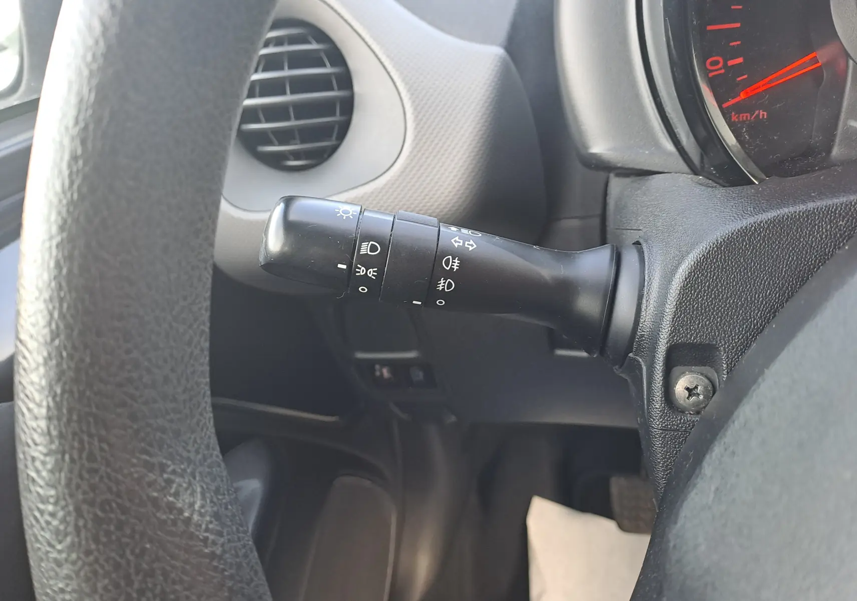 Gros plan sur la commande des phares à gauche du volant dans l’habitacle noir d’une Peugeot 108 Active 2020.