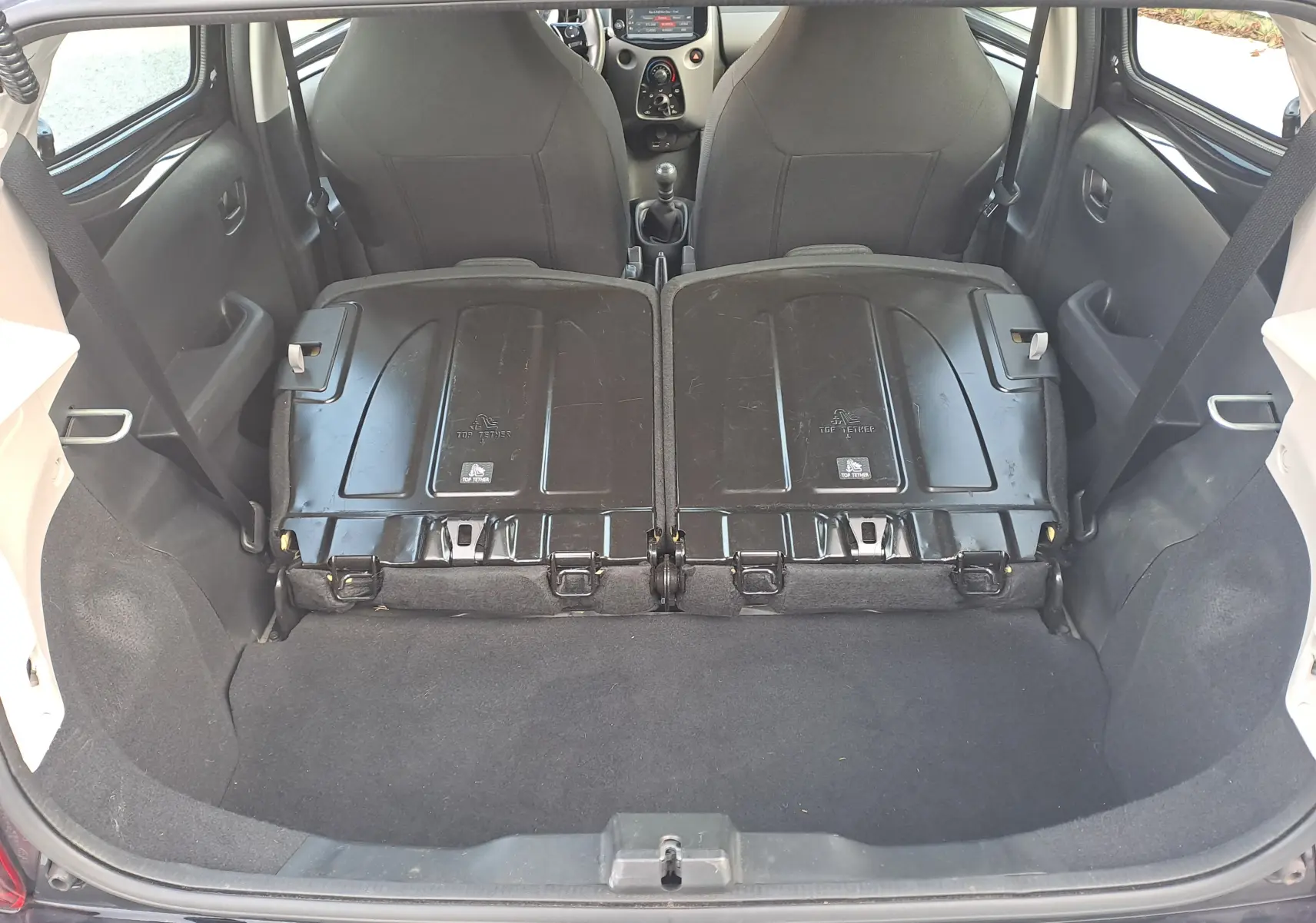 Coffre ouvert d'une Peugeot 108 noire, banquettes arrière rabattues vues de l'arrière offrant un espace de chargement plat.
