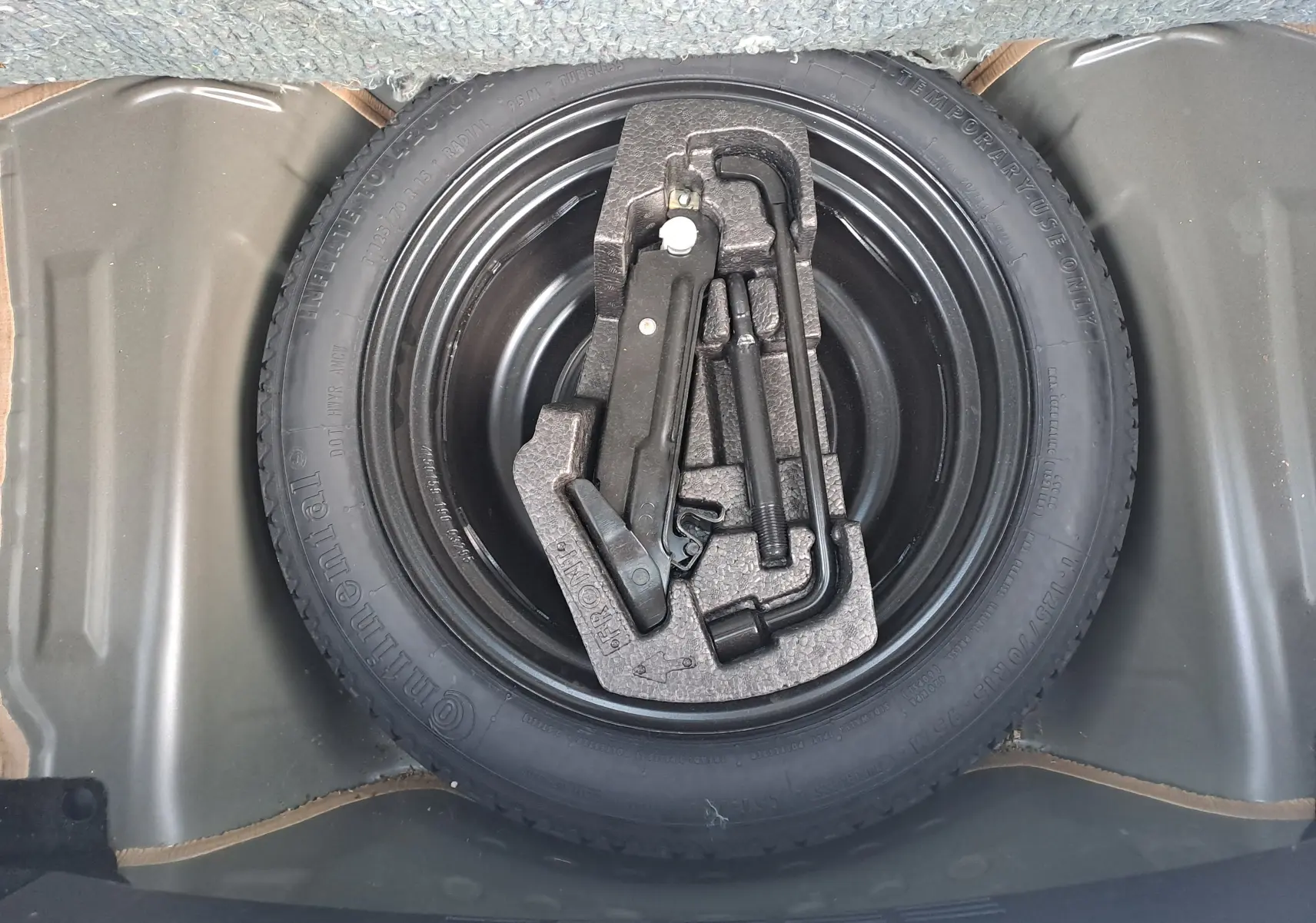 Vue plongeante sur la roue de secours noire d'une Peugeot 108 2020 avec kit de démontage intégré.