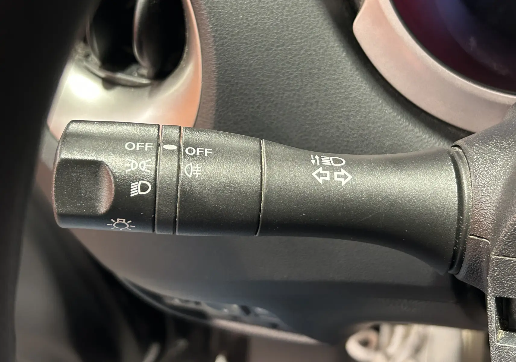 Gros plan sur la commande des clignotants et phares à gauche du volant dans un Nissan Juke noir métal de 2012.