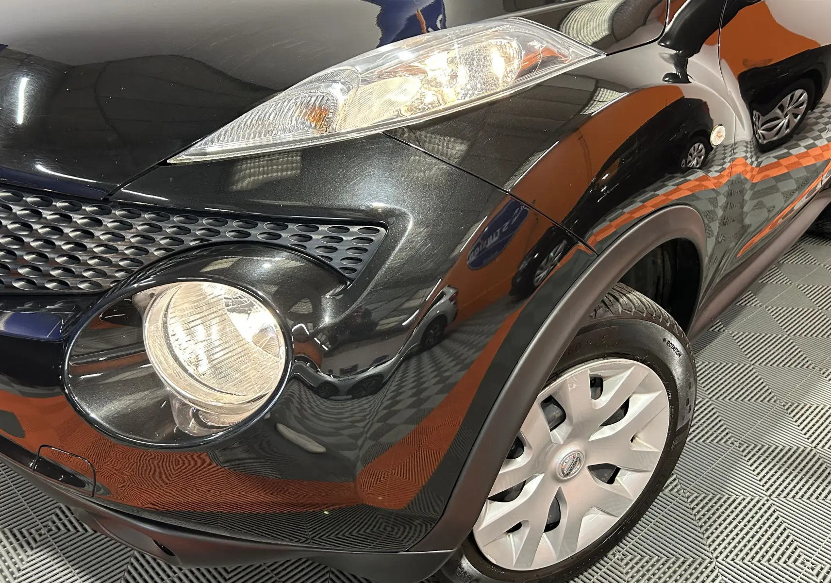 Gros plan sur l'avant droit noir métal du Nissan Juke 2012, mettant en valeur le phare rond et la calandre texturée.