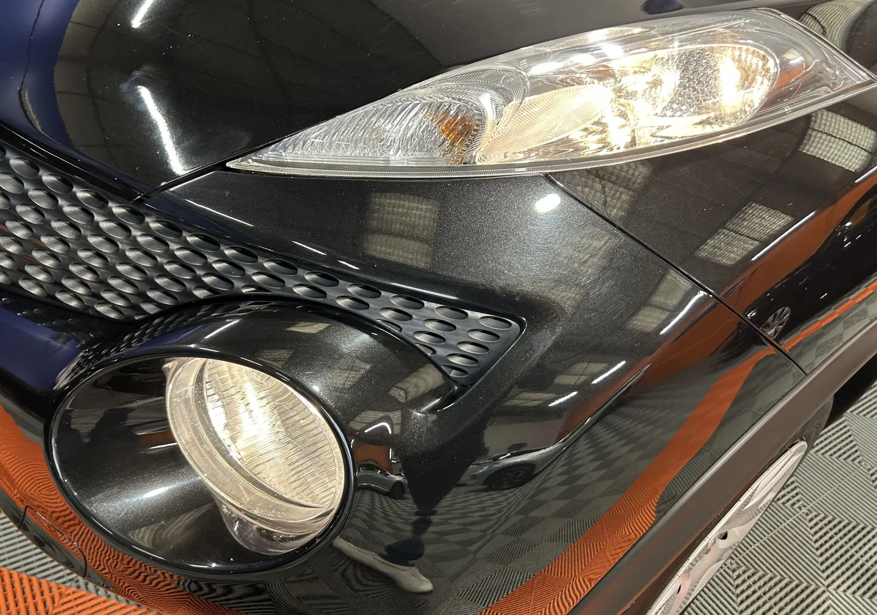 Gros plan sur l'avant droit noir métal du Nissan Juke 2012, mettant en valeur les phares et la calandre texturée.