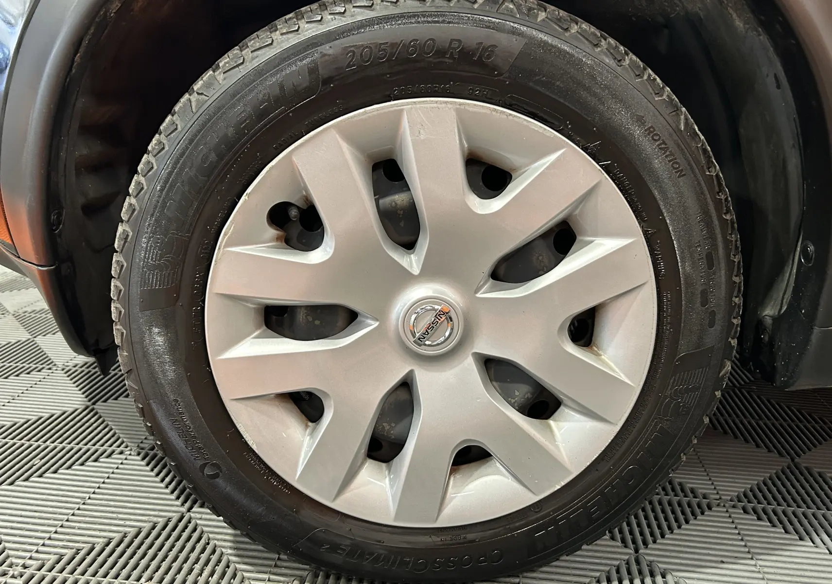 Gros plan sur la roue avant gauche d'un Nissan Juke noir métal, mettant en valeur le pneu Michelin et la jante avec enjoliveur gris.