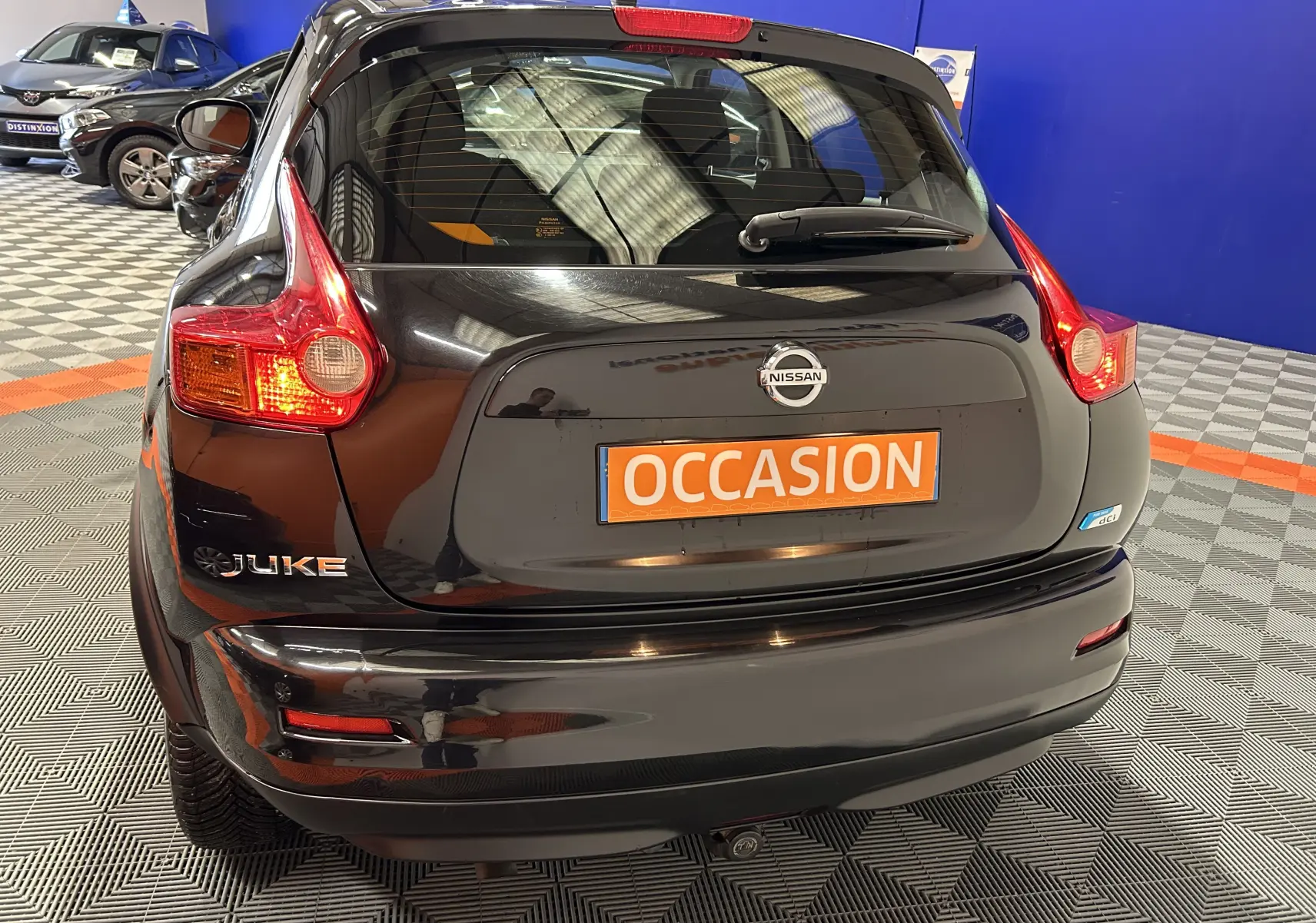 Vue arrière d'un Nissan Juke noir métal avec attelage, en intérieur sur sol damier gris et orange.
