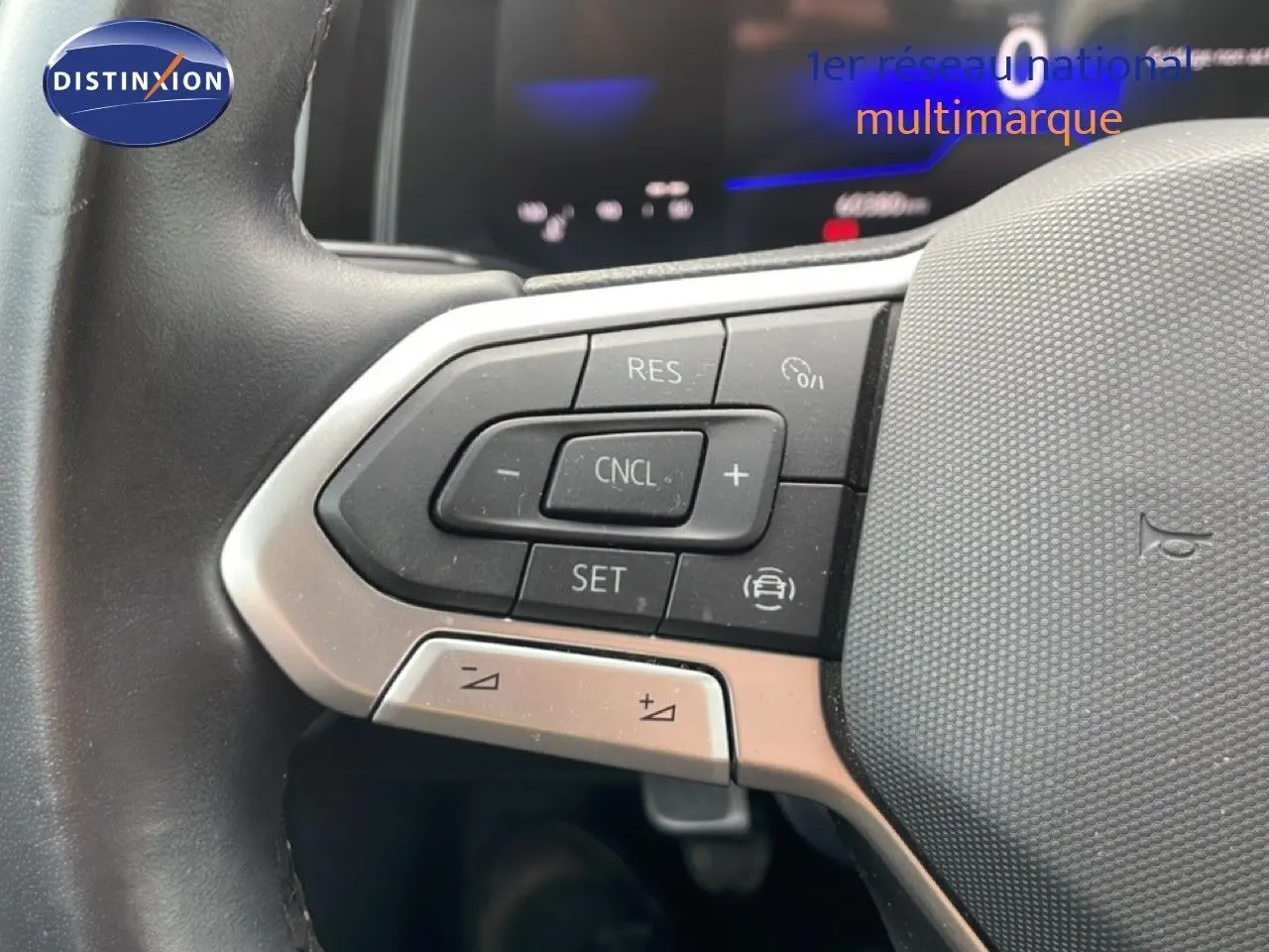Gros plan sur les commandes au volant à gauche d'une Volkswagen Polo blanche, avec boutons de régulateur de vitesse.