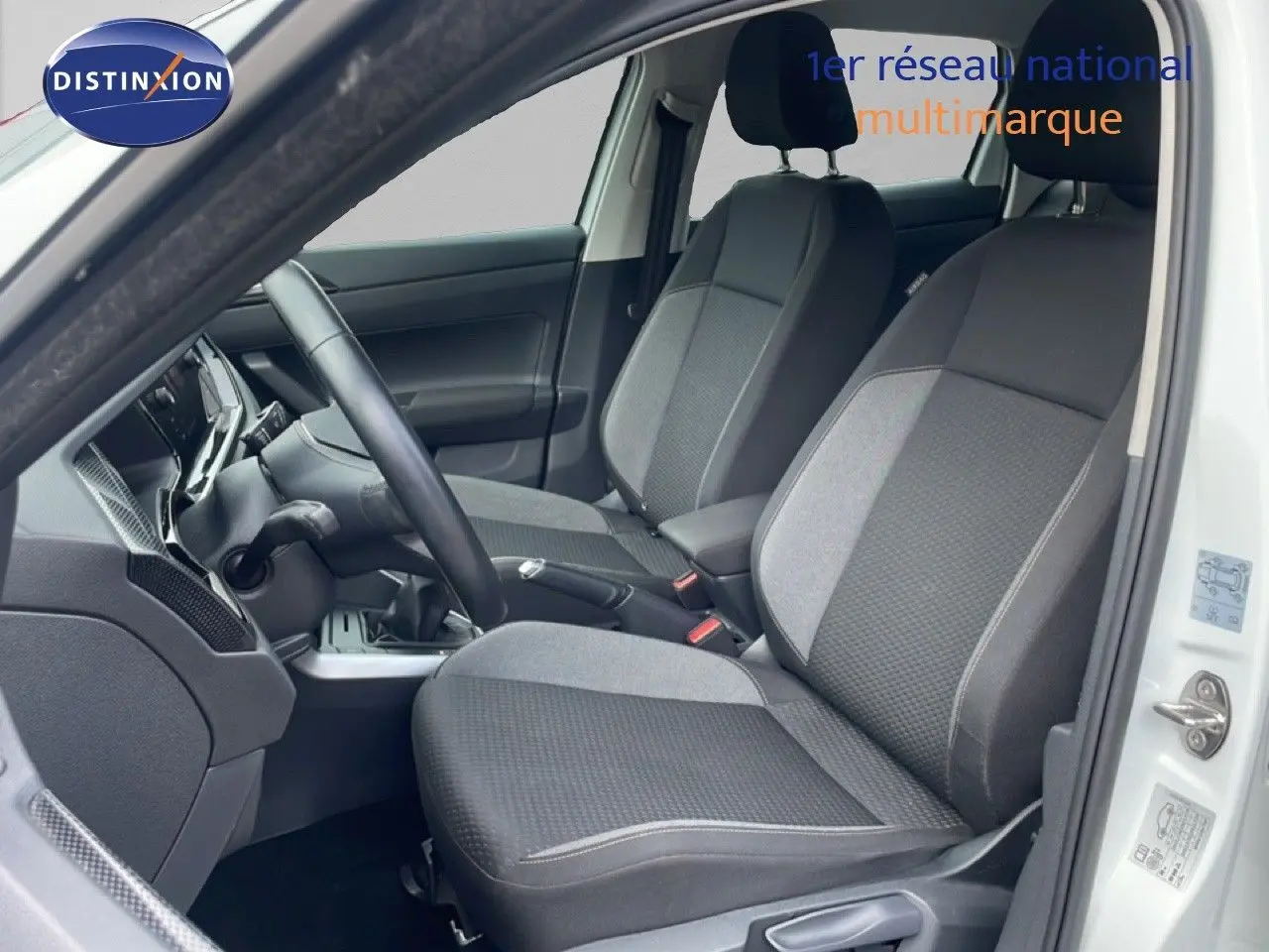 Vue intérieure côté conducteur de la Volkswagen Polo blanche 2022, mettant en valeur les sièges tissu gris et la boîte manuelle.