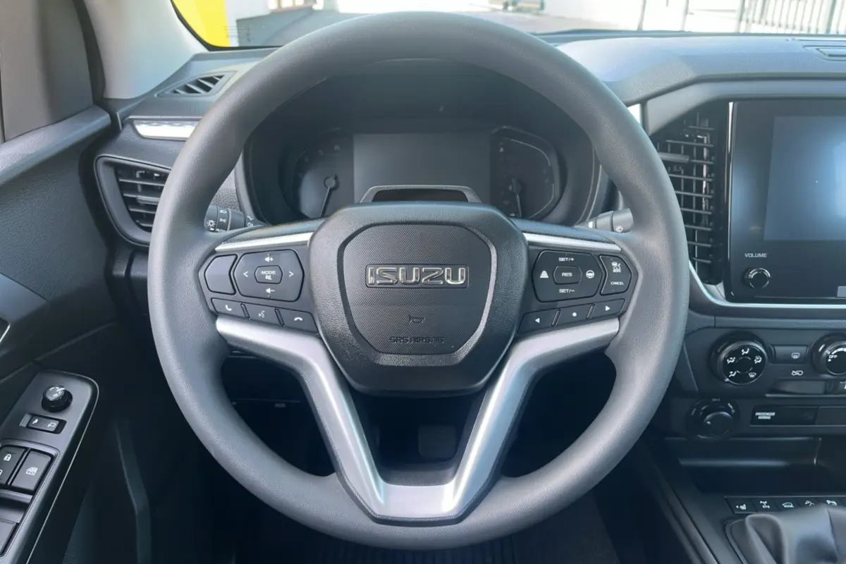 Vue rapprochée du volant multifonctions ISUZU D-MAX 2026 avec tableau de bord et écran tactile à droite.