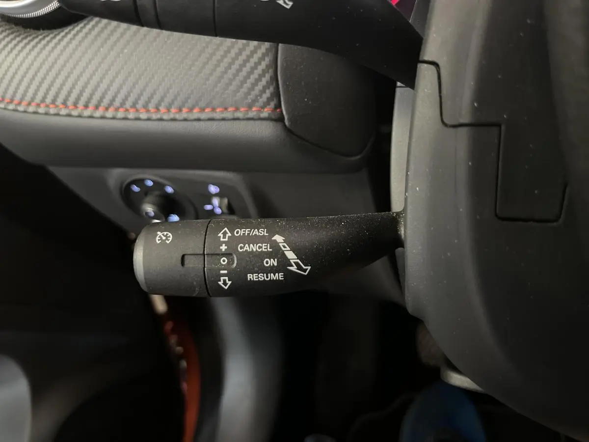 Gros plan sur la commande de régulateur de vitesse à gauche du volant dans l’habitacle noir et tissu du MG ZS orange.