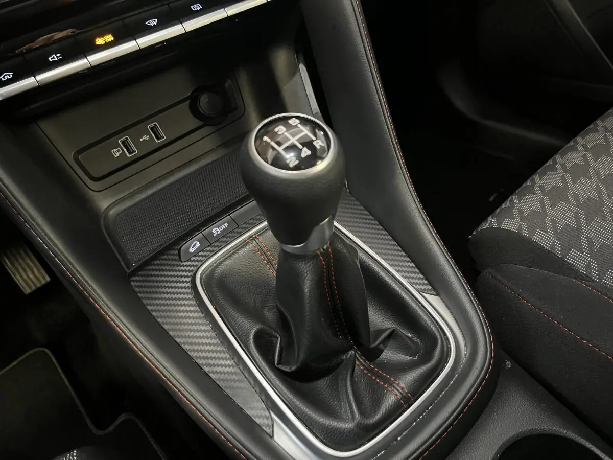 Le levier de vitesse manuel en cuir noir avec surpiqûres orange du MG ZS 1.5L VTi Tech, entouré d'un habillage effet carbone.