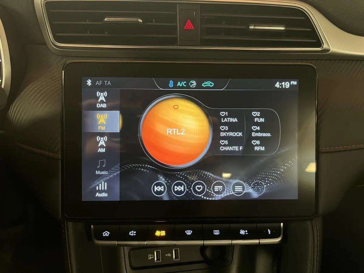Écran tactile central allumé affichant la radio FM dans l'habitacle du MG ZS 1.5L Tech orange.