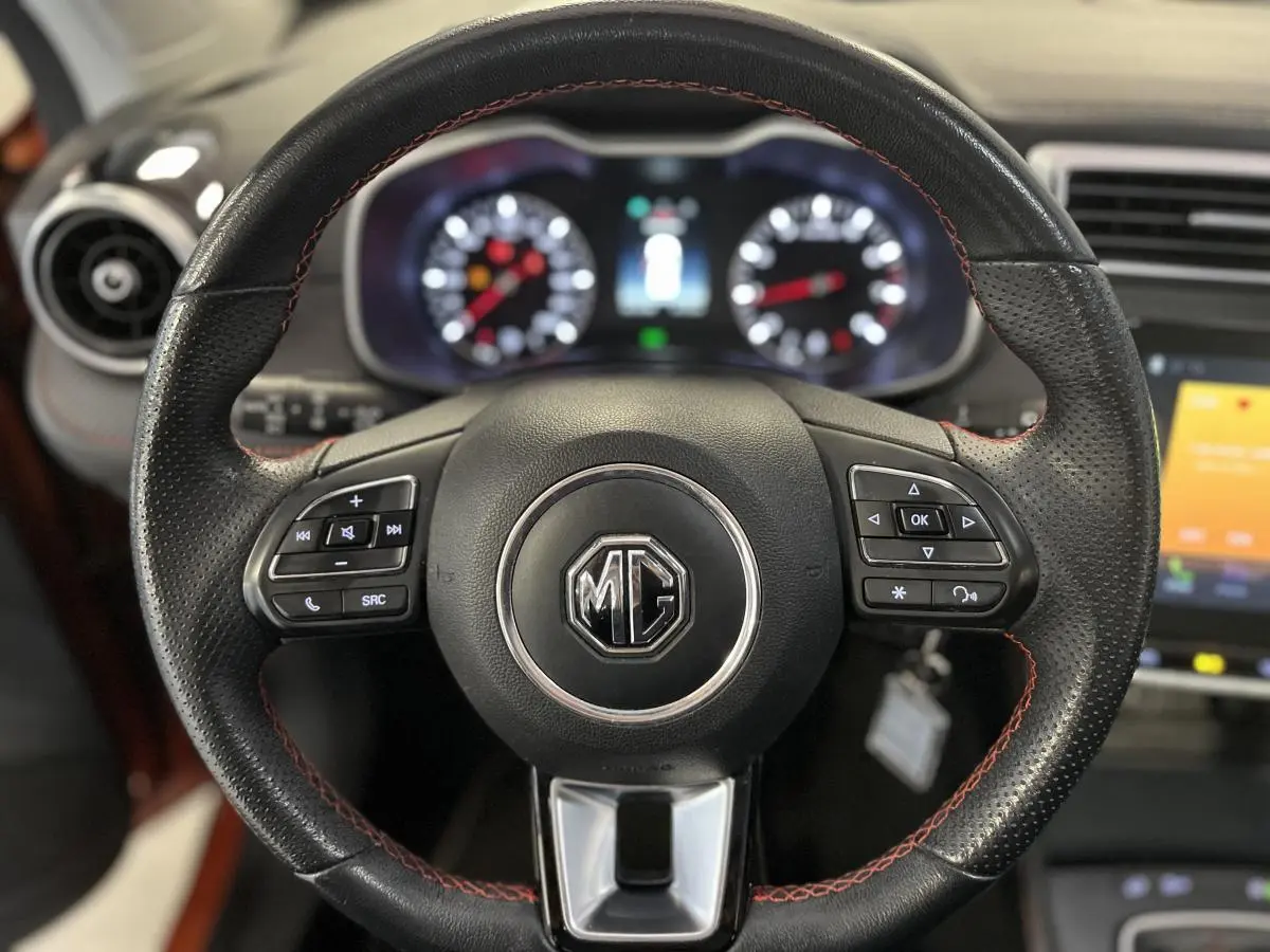 Volant en cuir noir avec surpiqûres rouges du MG ZS 2022, tableau de bord et écran tactile en arrière-plan flous.