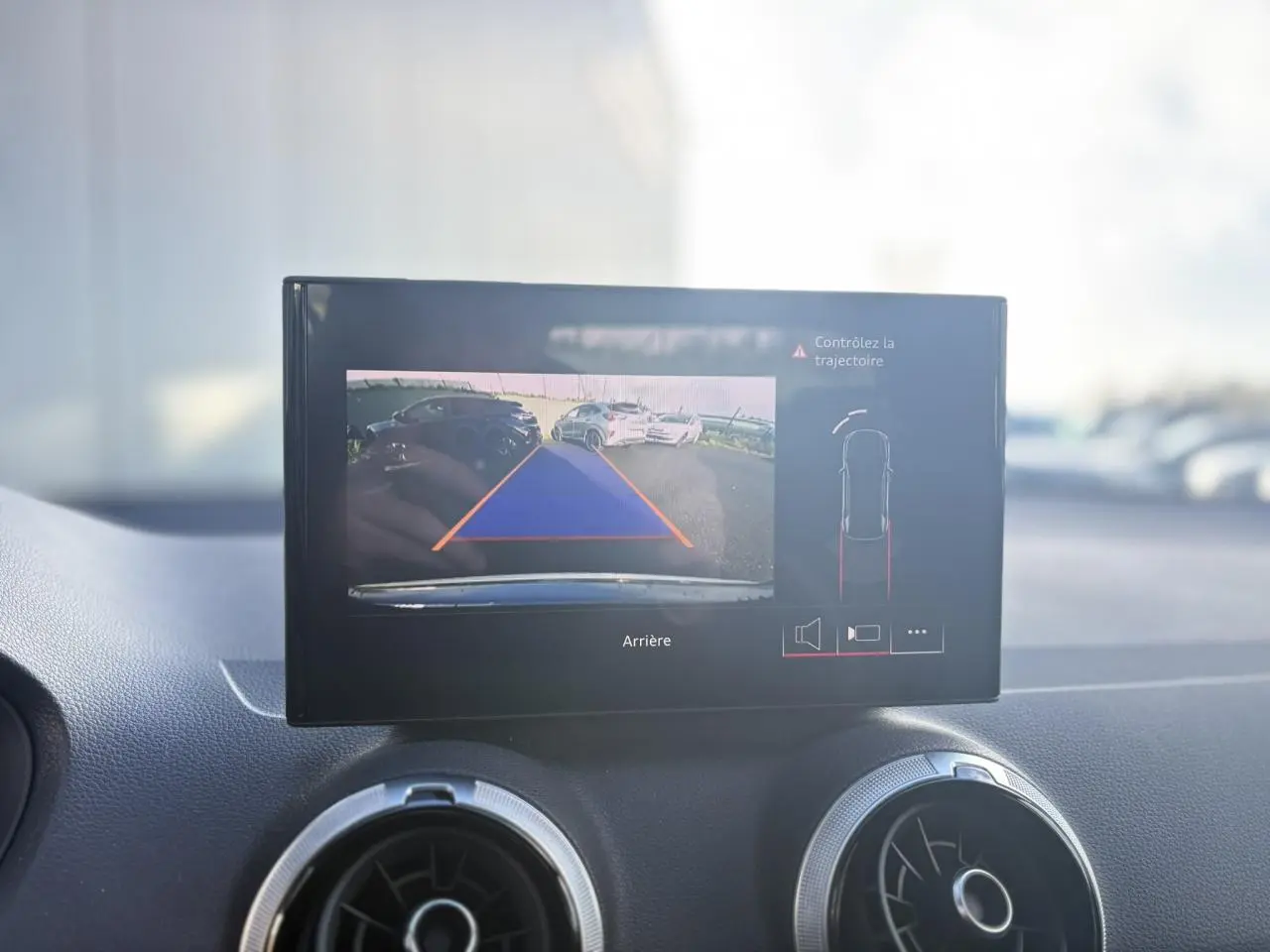 Écran central affichant la caméra de recul et l'aide au stationnement dans un Audi Q2 gris Daytona, vue intérieure.