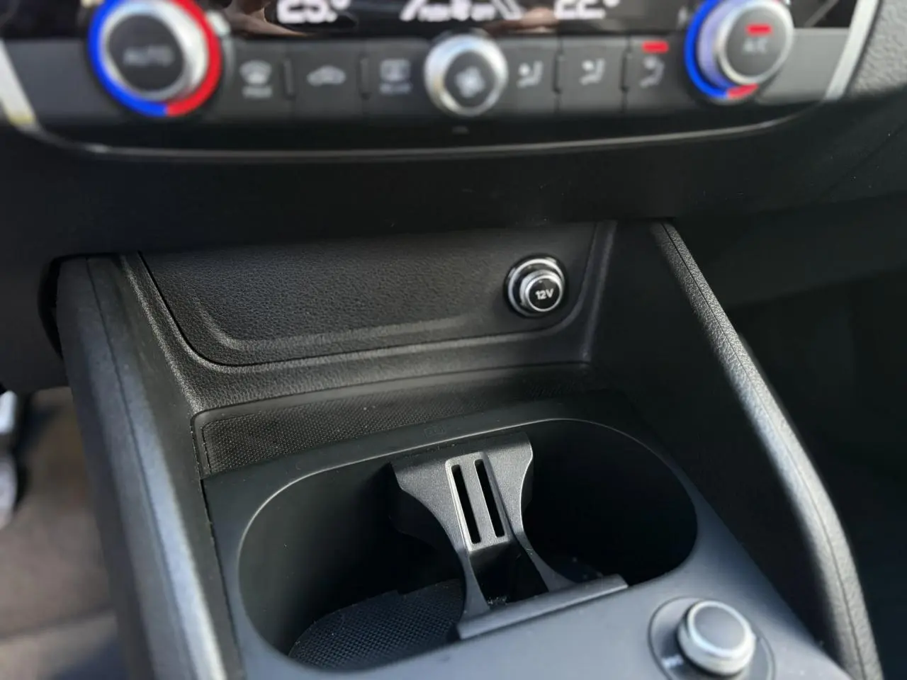 Gros plan sur la console centrale de l'Audi Q2 30 TDI S-Line 2025, montrant les porte-gobelets et prise 12V.