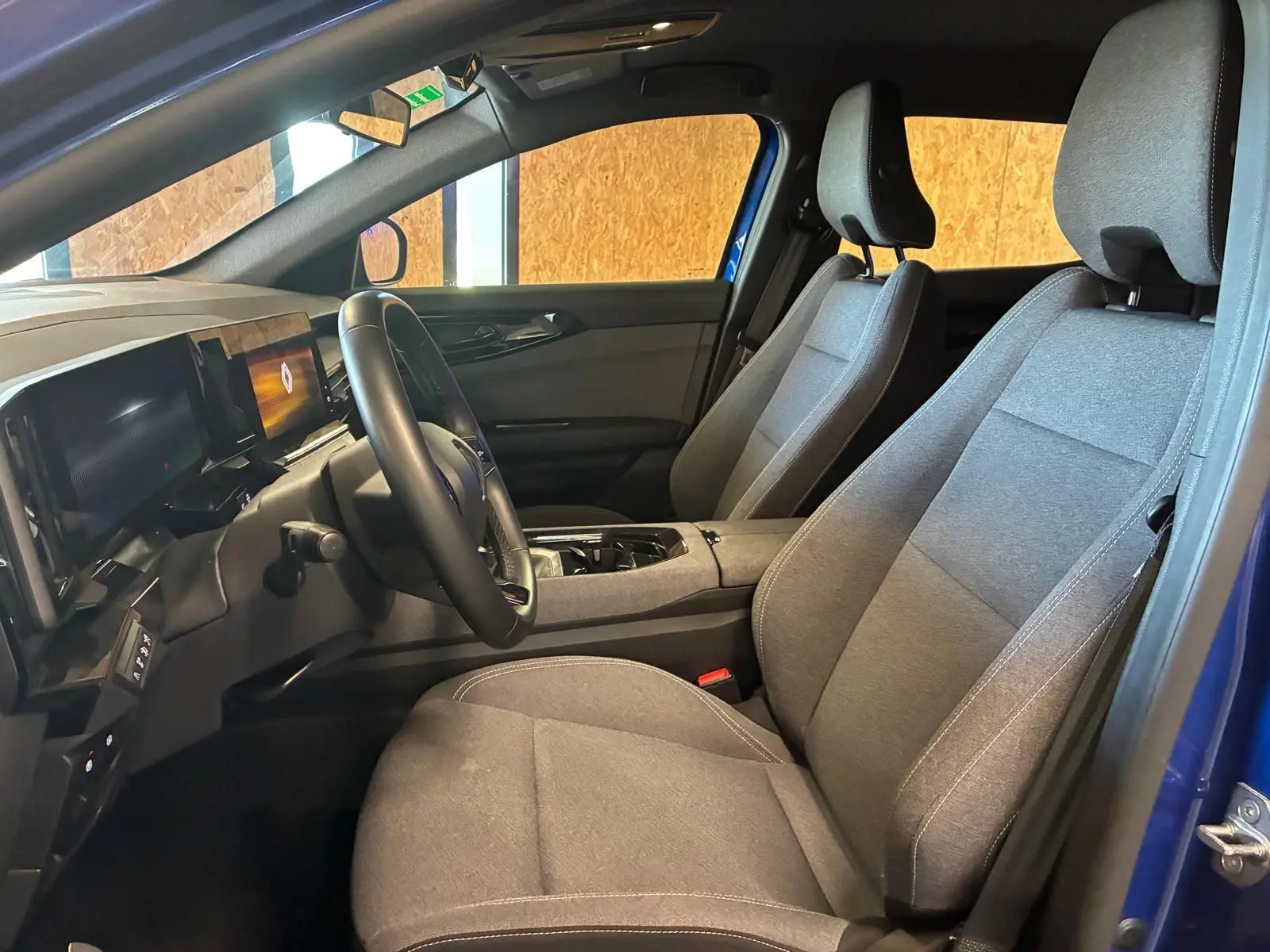 Vue intérieure côté conducteur du Renault Austral bleu 2024, sièges tissu gris et tableau de bord moderne avec écran digital.