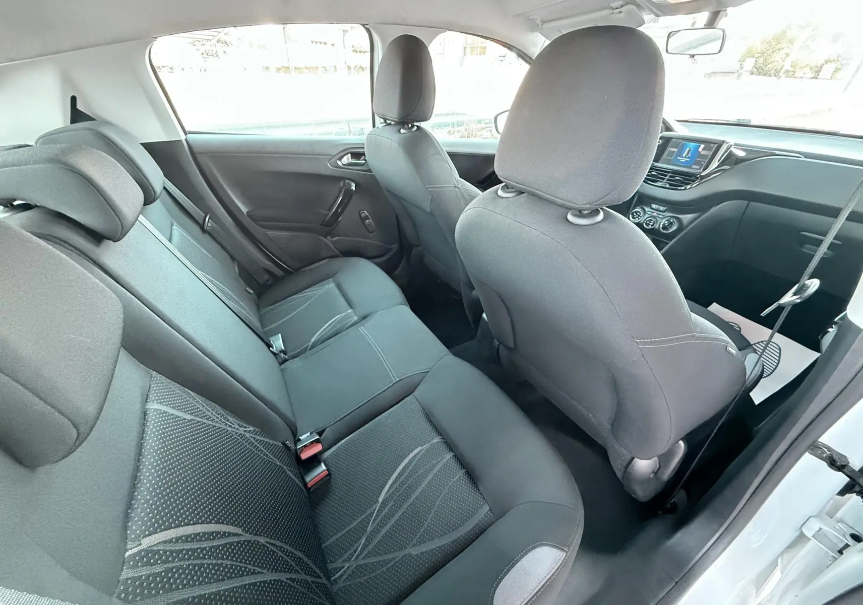 Vue intérieure arrière côté droit de la Peugeot 208 blanche de 2013, montrant les sièges noirs et la console avant.