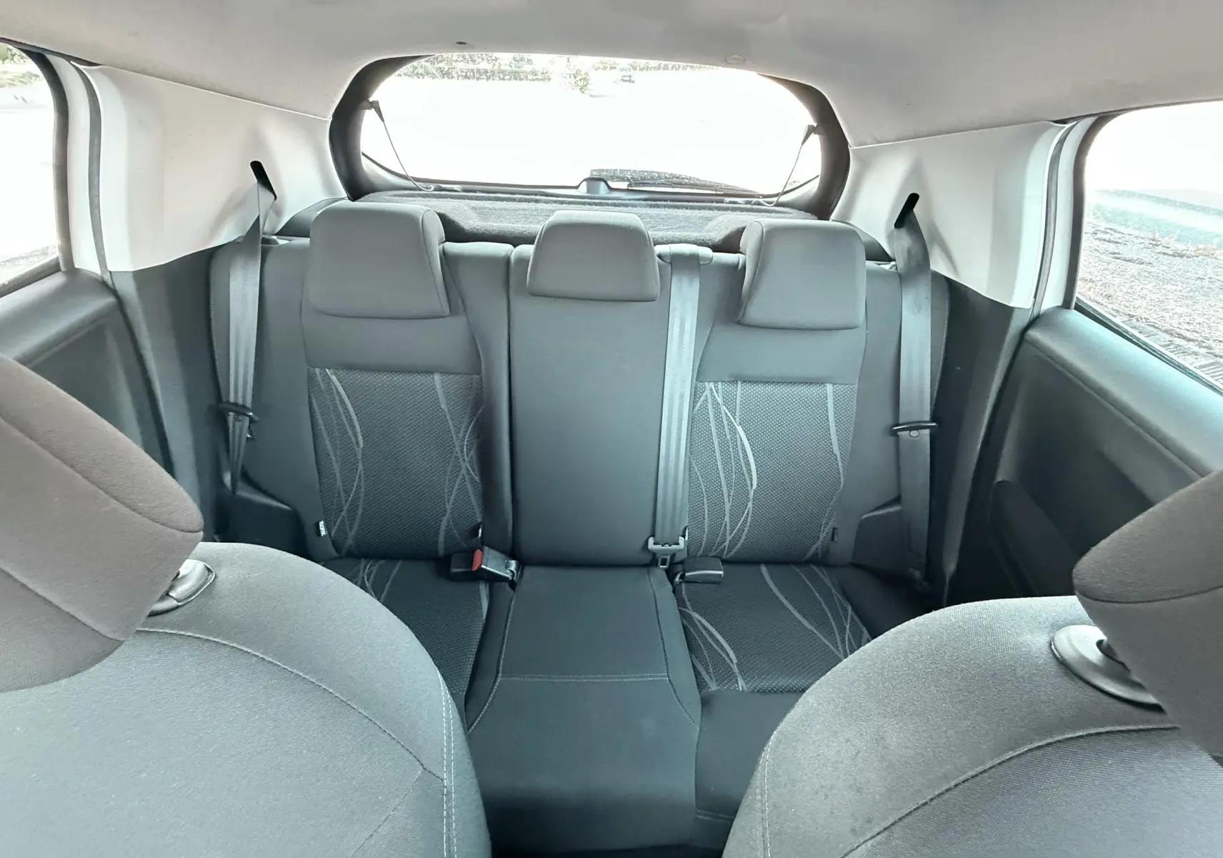 Vue intérieure arrière montrant les sièges arrière noirs avec motifs gris d'une Peugeot 208 blanche de 2013.