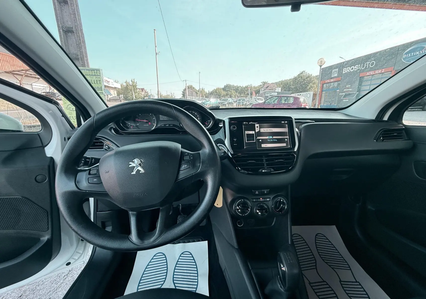 Vue intérieure avant de la Peugeot 208 blanche 2013, montrant le volant, tableau de bord et console centrale avec écran tactile.