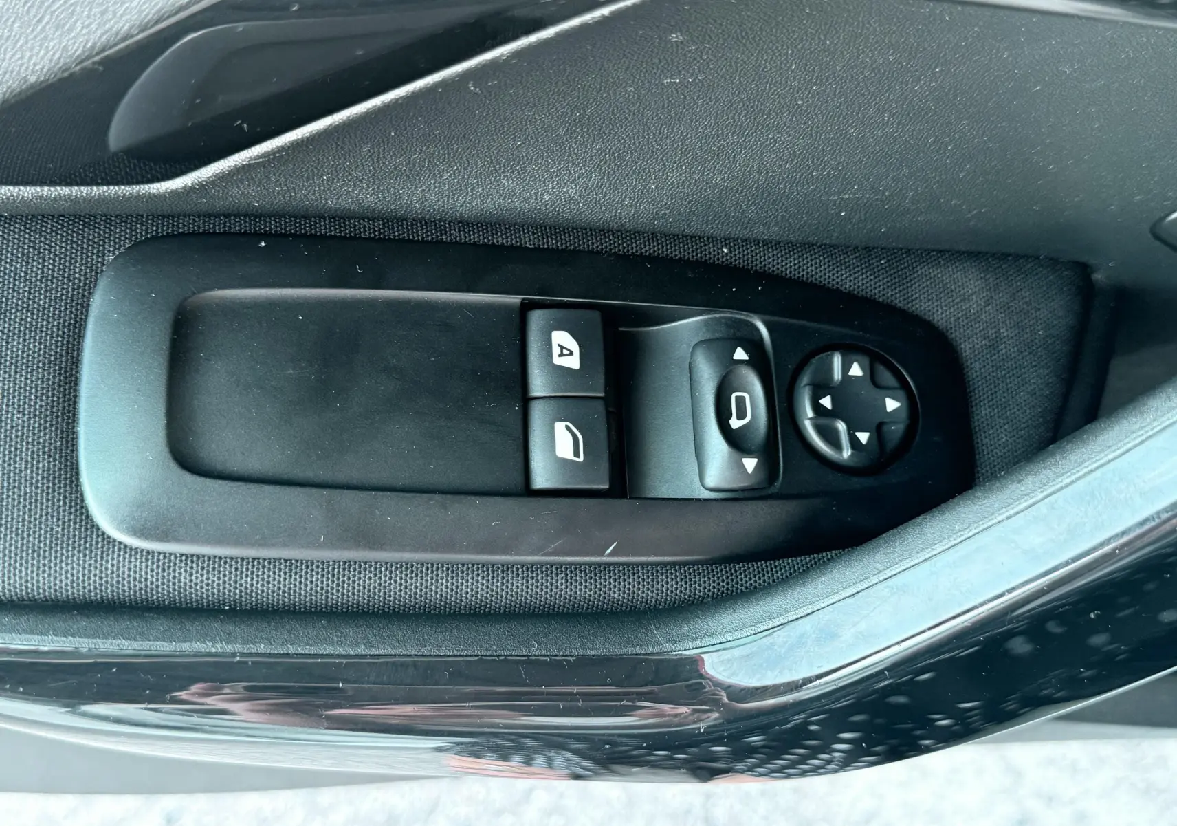 Gros plan sur les commandes de lève-vitres et réglage des rétroviseurs côté conducteur d'une Peugeot 208 blanche de 2013.