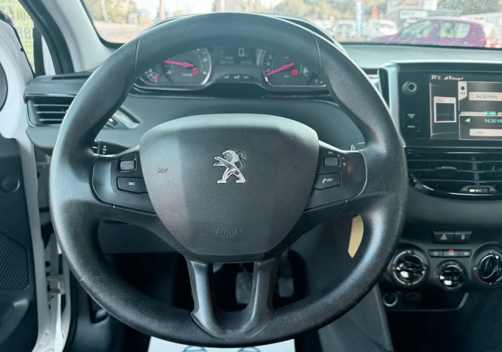 Vue rapprochée du volant noir de la Peugeot 208 blanche 1.4 HDi 2013 avec tableau de bord et console centrale visibles.