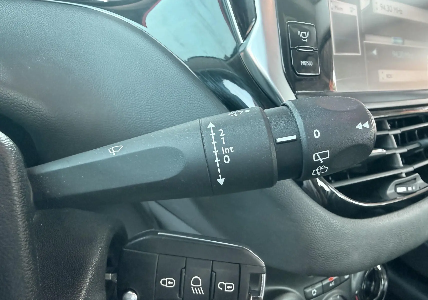 Gros plan sur la commande d’essuie-glace à gauche du volant dans l’habitacle noir d’une Peugeot 208 blanche de 2013.