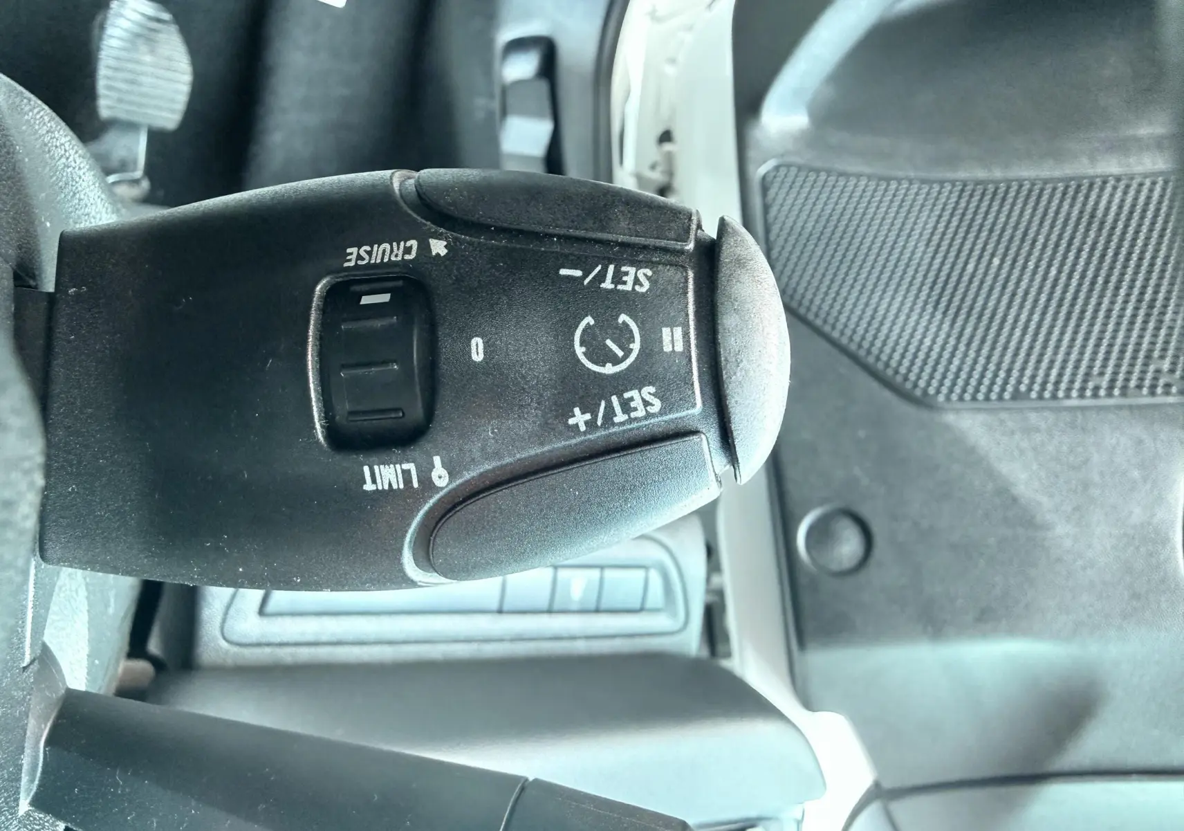 Gros plan sur la commande de régulateur de vitesse noire dans l’habitacle d’une Peugeot 208 blanche de 2013.