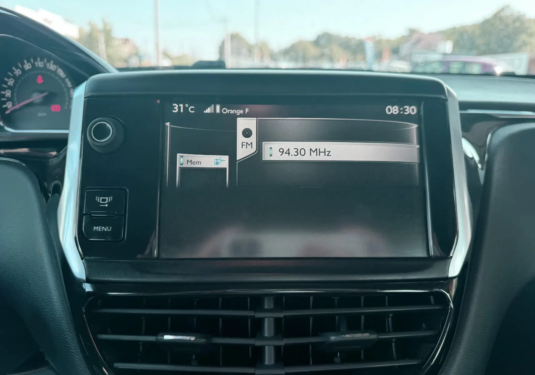 Écran central tactile du tableau de bord d’une Peugeot 208 blanche de 2013 affichant la radio FM à 94,30 MHz.