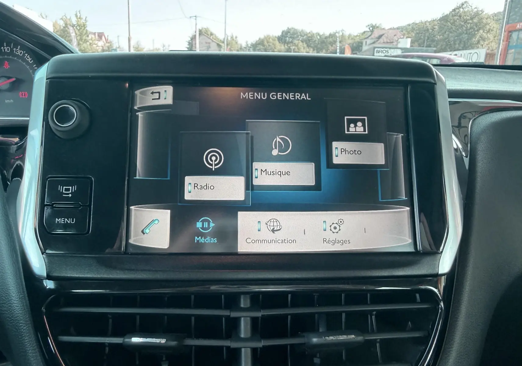 Vue rapprochée de l'écran tactile central du tableau de bord d'une Peugeot 208 blanche, affichant le menu général multimédia.