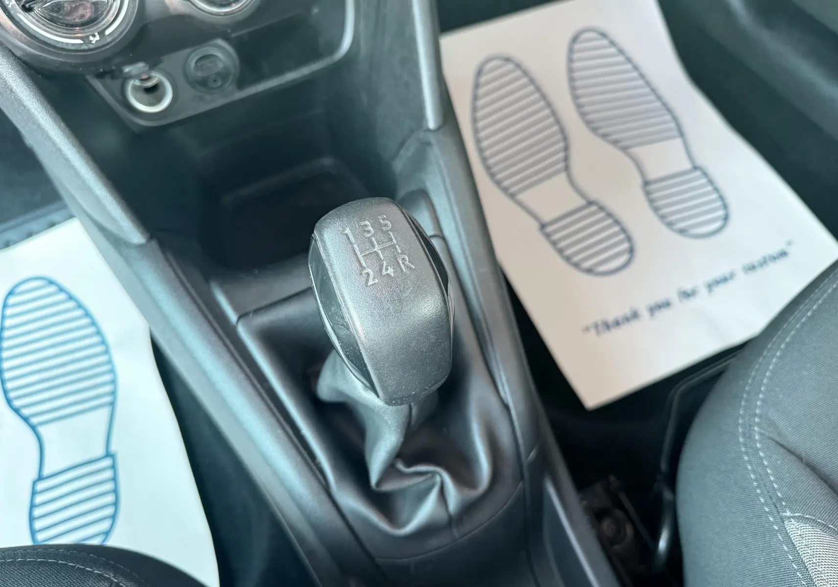 Vue rapprochée du levier de vitesses manuel noir dans l’habitacle d’une Peugeot 208 blanche de 2013.