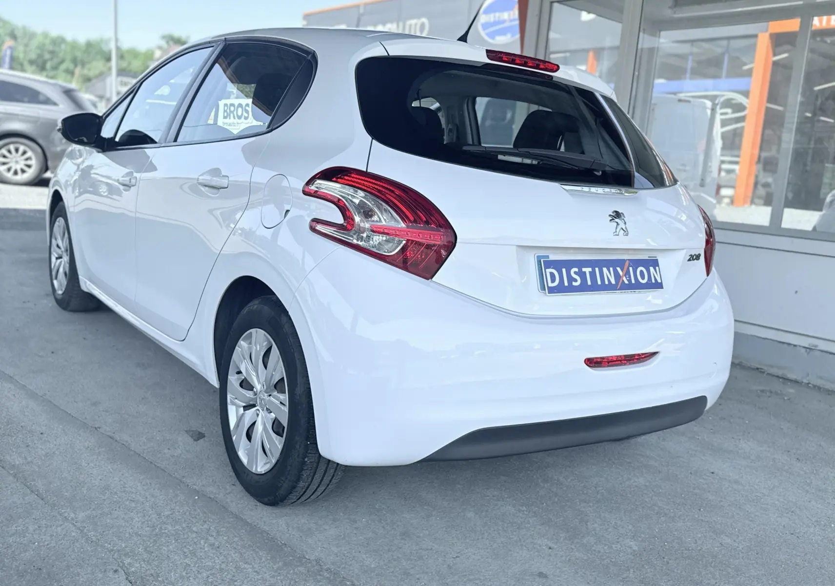 Peugeot 208 blanc vue 3/4 arrière droit, avec feux arrière distinctifs et logo lion sur hayon.
