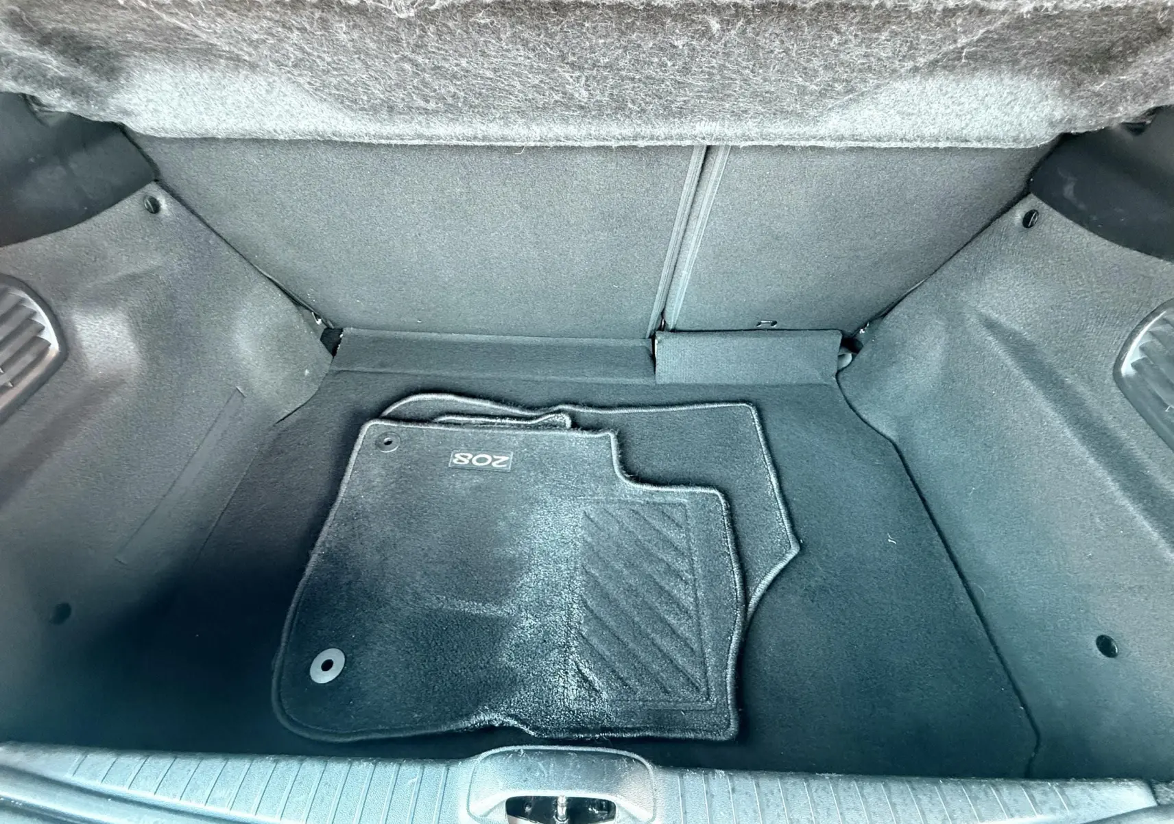 Coffre de Peugeot 208 blanc, vue plongeante sur tapis de sol noir marqué 208, intérieur propre et vide.