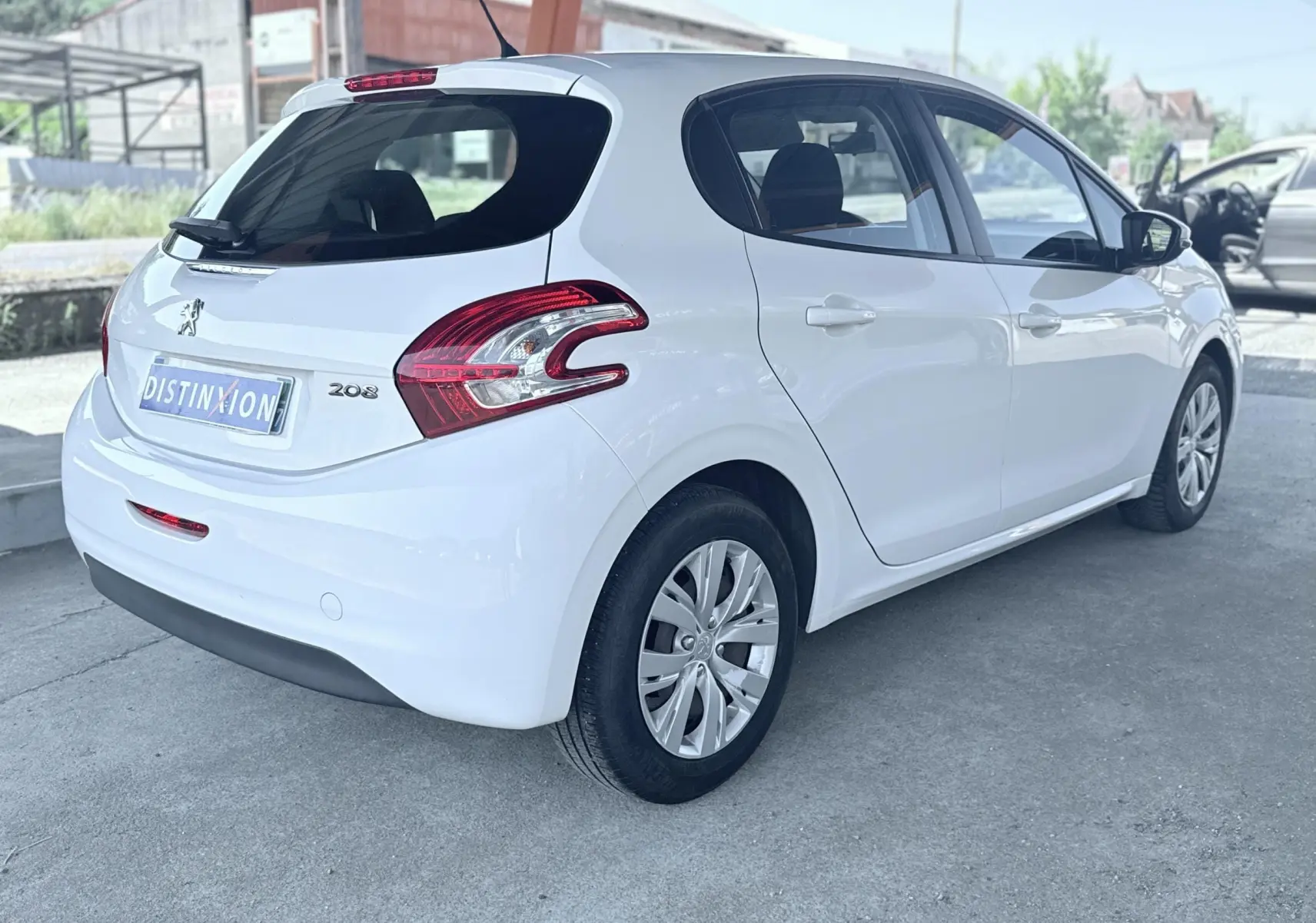 Peugeot 208 blanc vue 3/4 arrière droit, avec feux arrière distinctifs et jantes alliage, porte avant droite ouverte.