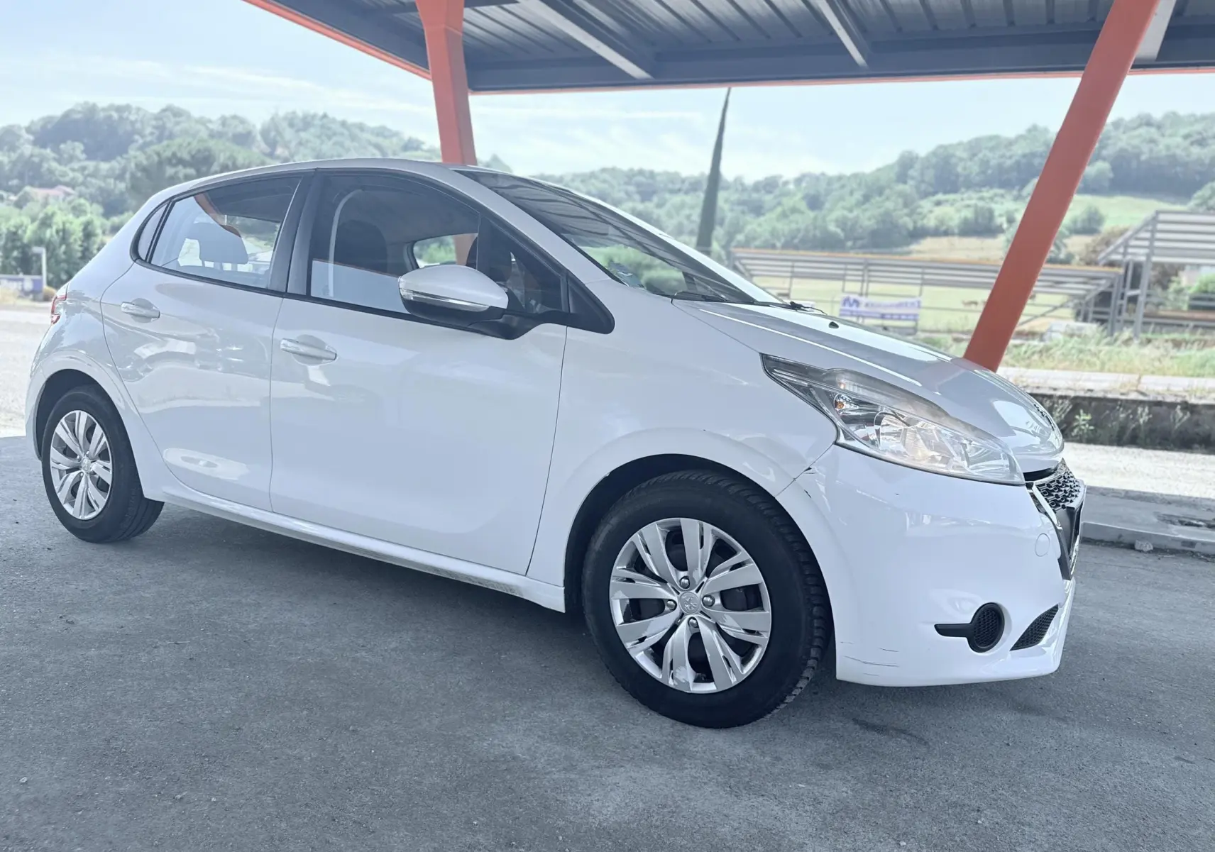 Peugeot 208 blanche vue de profil droit sous abri, avec jantes alliage et phares avant distinctifs.