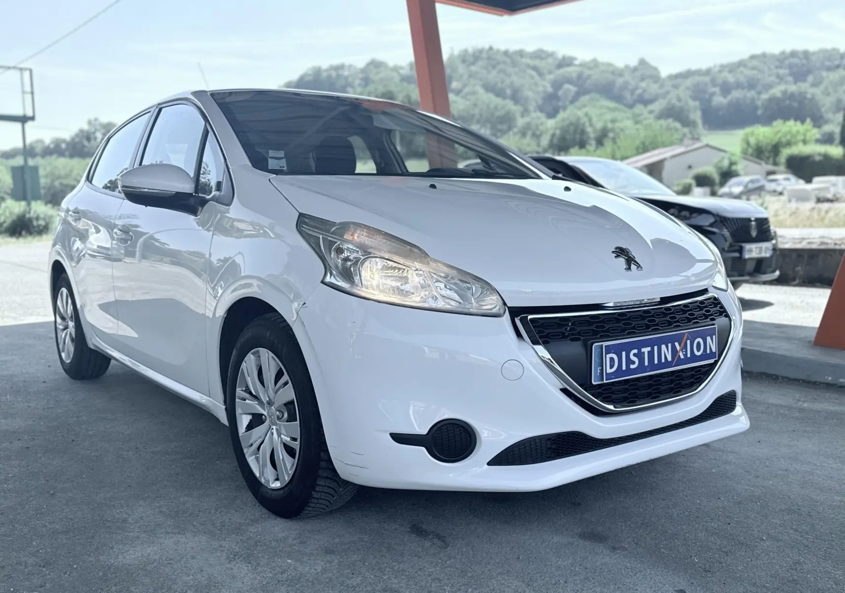 Peugeot 208 blanc vue 3/4 avant droit sous abri, avec calandre noire et plaque d'immatriculation Distinxion.