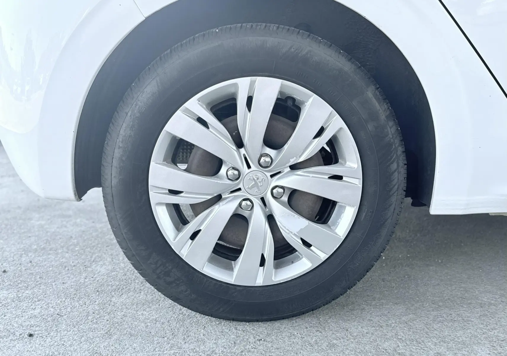 Gros plan sur la roue arrière droite blanche d'une Peugeot 208 1.4 HDi 70ch Active de 2013 avec jante alliage argentée.