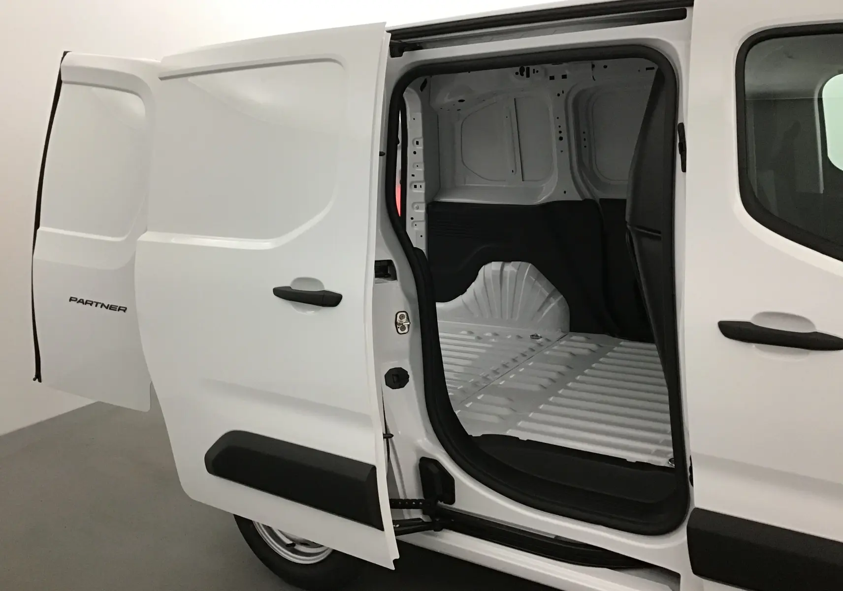 Vue latérale droite d'un utilitaire Peugeot Partner blanc avec porte coulissante ouverte révélant l'espace de chargement vide.