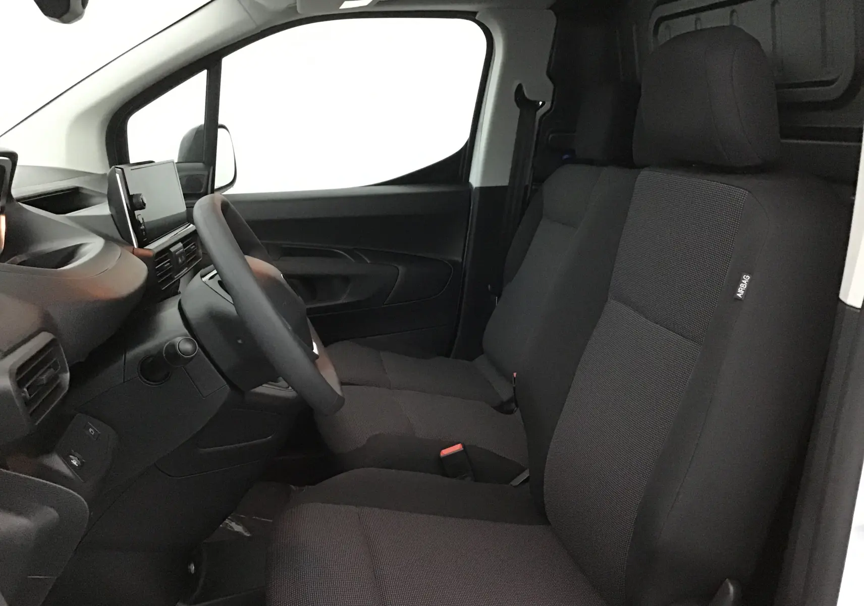 Vue intérieure côté conducteur du Peugeot Partner blanc, montrant les sièges avant en tissu noir et le tableau de bord moderne.